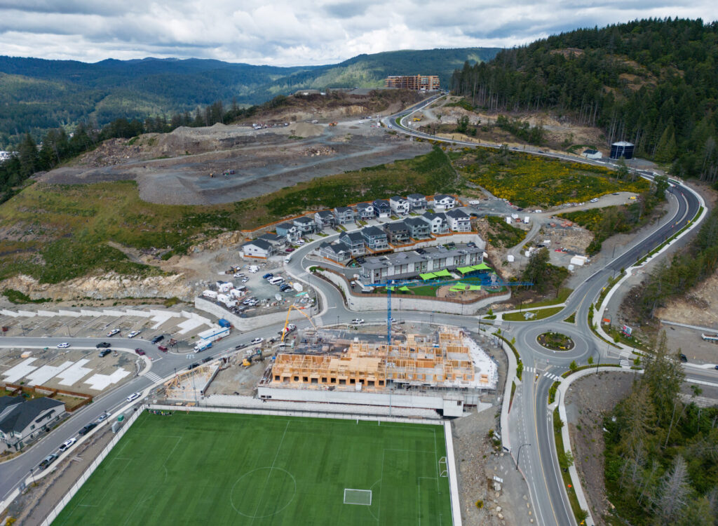 Le complexe d’appartements se trouve à côté d’un terrain de football carré et vert. Les maisons situées derrière le complexe se trouvent sur une route incurvée, juste à côté d’une autoroute avec un rond-point. Le terrain a été défriché sur la colline derrière les maisons. Plus loin, on aperçoit un immeuble d’habitation de faible hauteur. Au-delà, des collines couvertes de forêts.